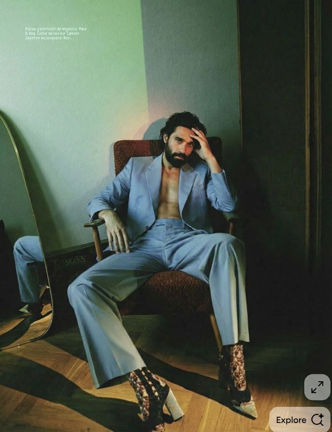 Amos Le Blanc in an open light blue suit seated in an armchair beside a mirror