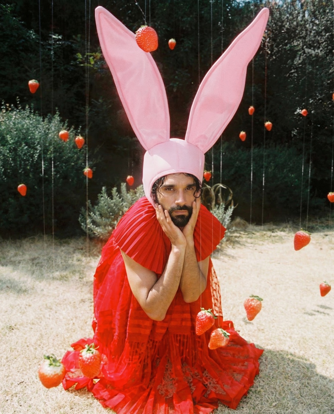 Amos Le Blanc kneeling in pink bunny ears and red pleats among hanging strawberries