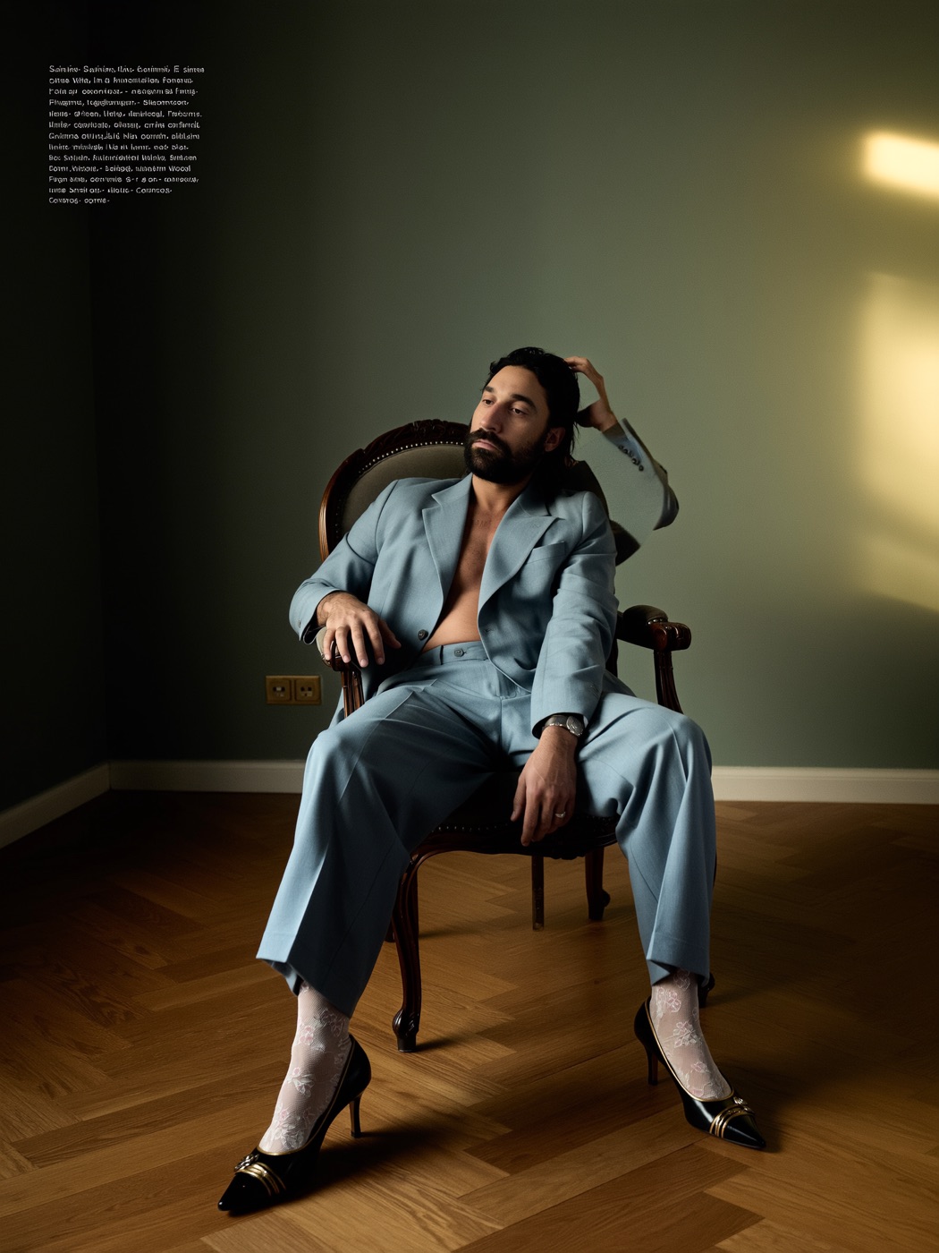 Amos Le Blanc in an open pale blue suit seated in an ornate chair wearing lace socks and heels