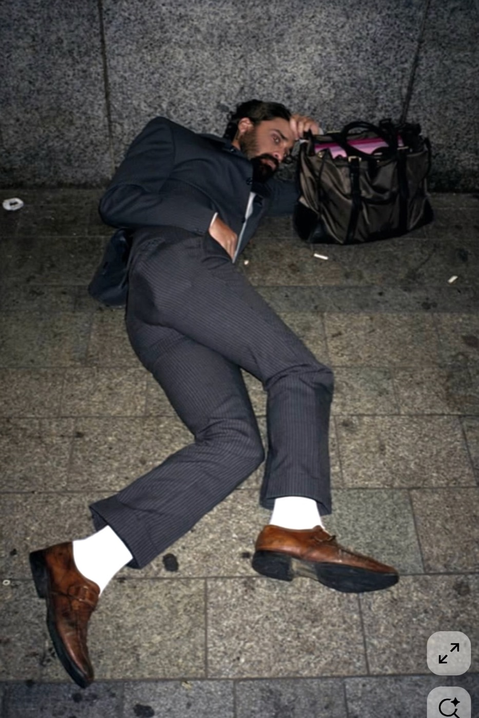 Amos Le Blanc in a pinstripe suit lying on night pavement beside a duffel bag